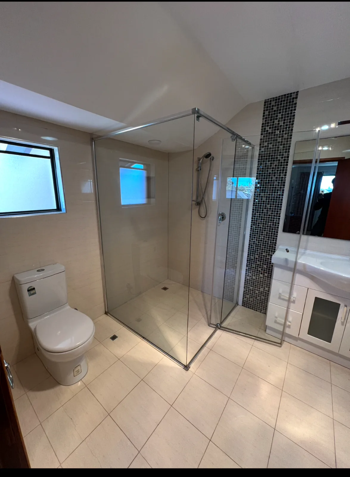 Clean bathroom with a frameless glass shower screen, a dark mosaic feature strip, toilet and vanity