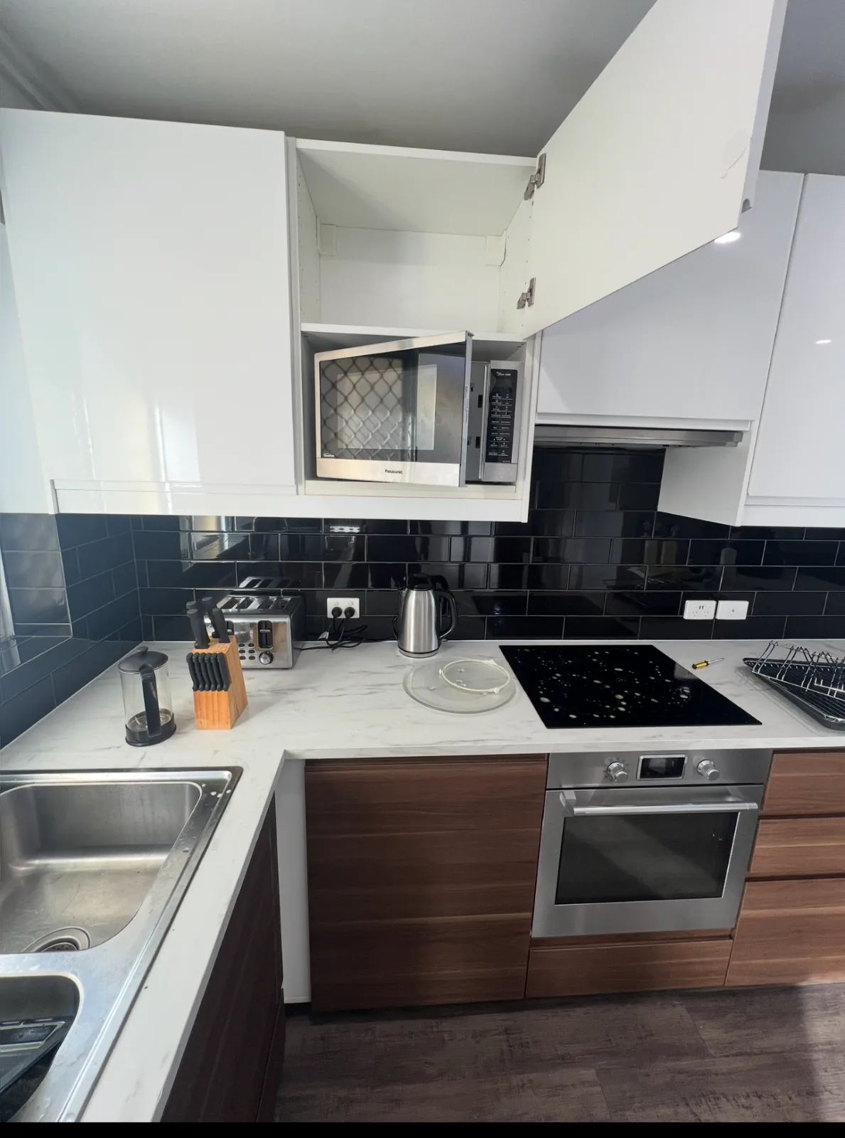 Clean kitchen with a black gloss subway tile splashback, marble look benchtop and an empty overhead cabinet standing open
