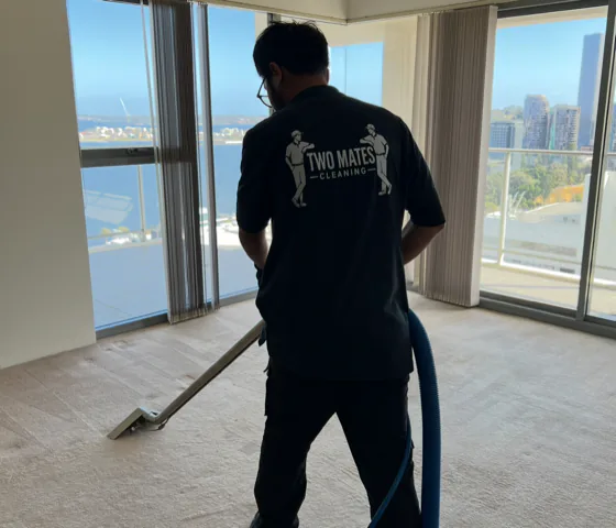 Two Mates Cleaning team member in branded uniform cleaning carpet in an empty apartment