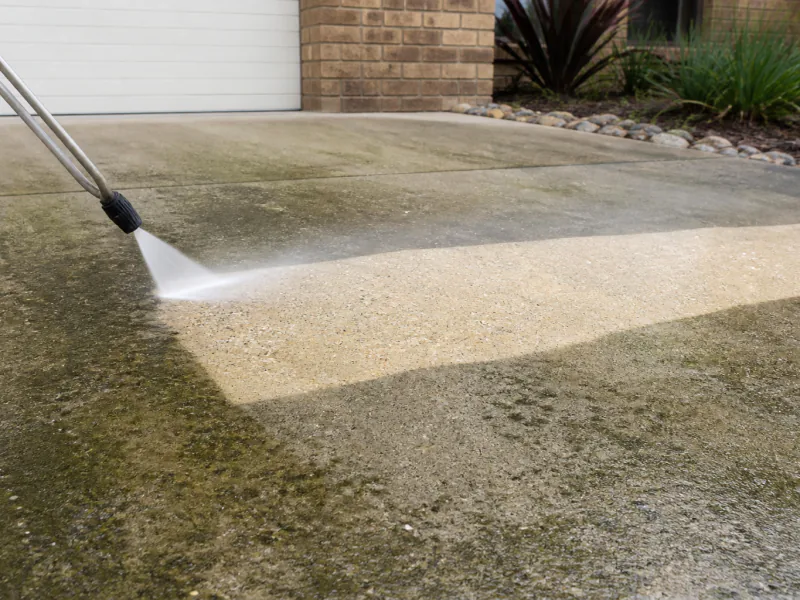 A concrete driveway being pressure washed, showing a clean stripe against the weathered surface