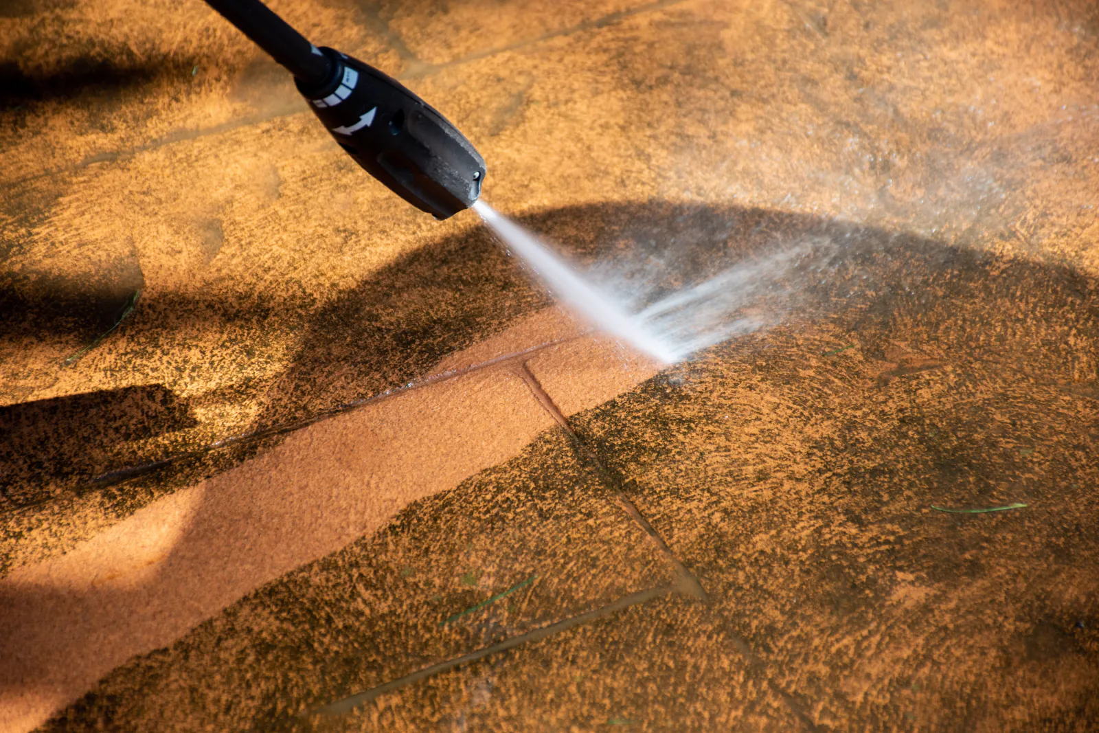 Pressure washing equipment in use, spraying a fan of water across a stained paved surface