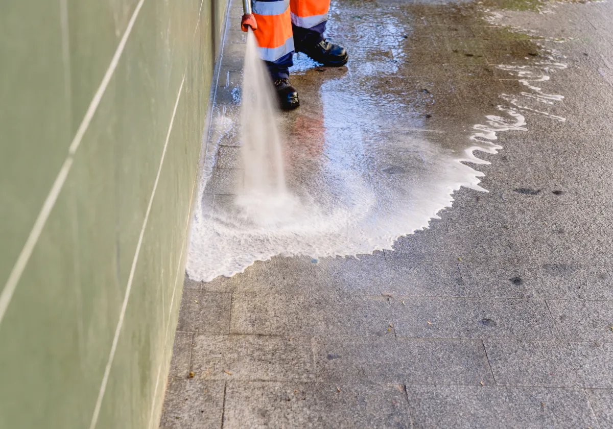 A pressure washer spraying a fan of water across a stained paved surface