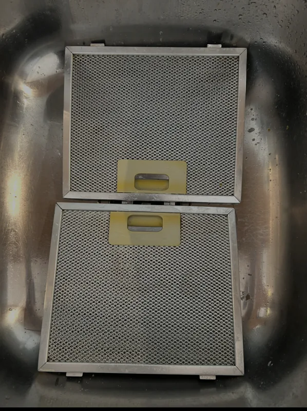 The same two rangehood mesh filters after cleaning, back to bare silver mesh in a stainless steel sink