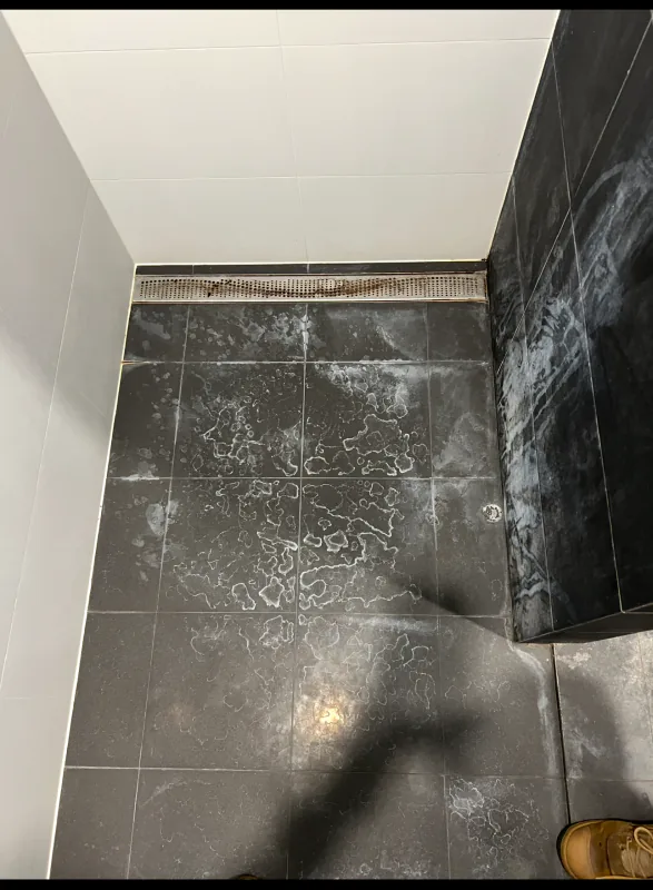 Dark charcoal shower floor tiles covered in white soap scum and mineral deposits before cleaning