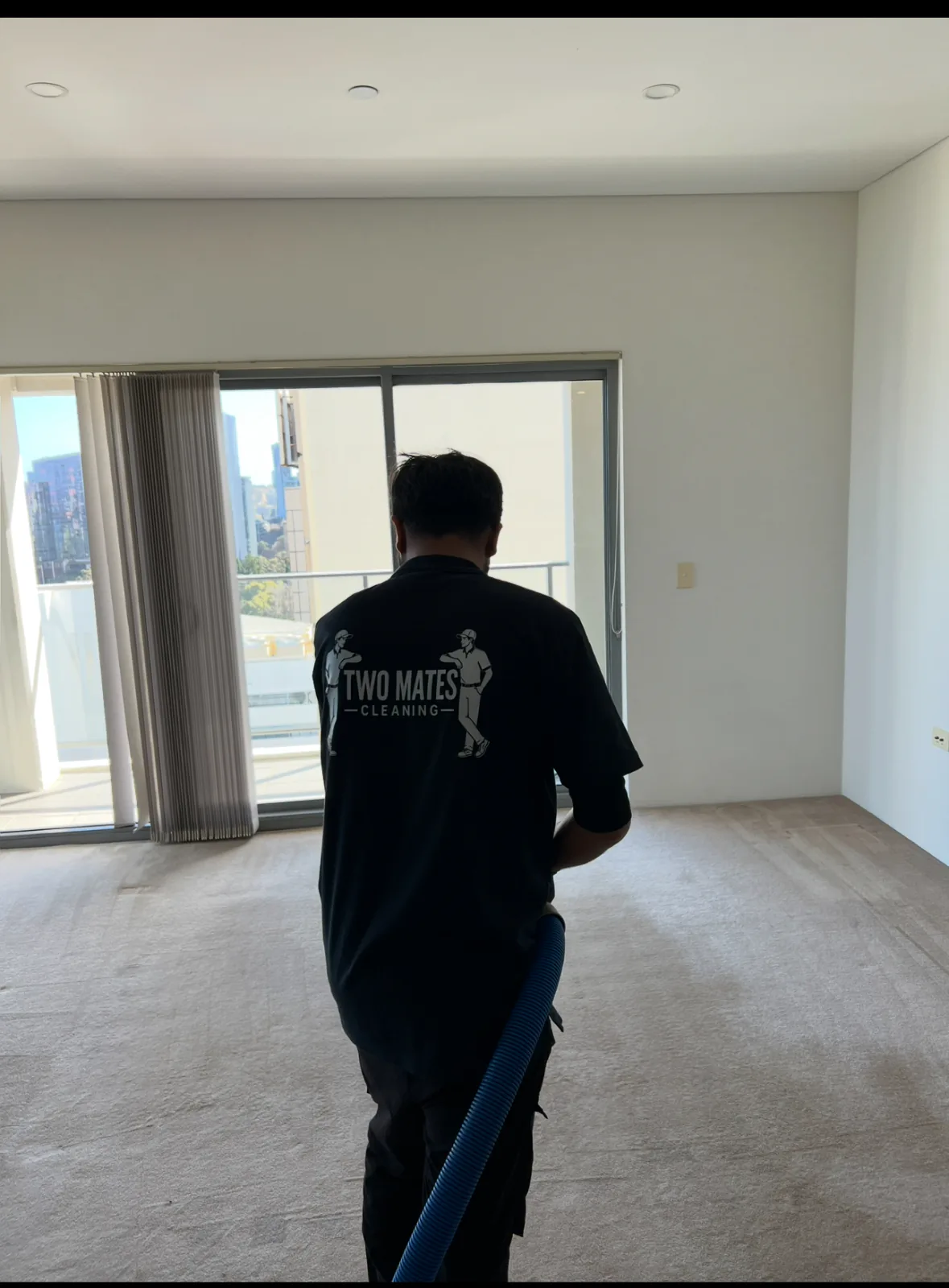 Two Mates Cleaning team member in branded uniform using a carpet extraction machine in an empty apartment
