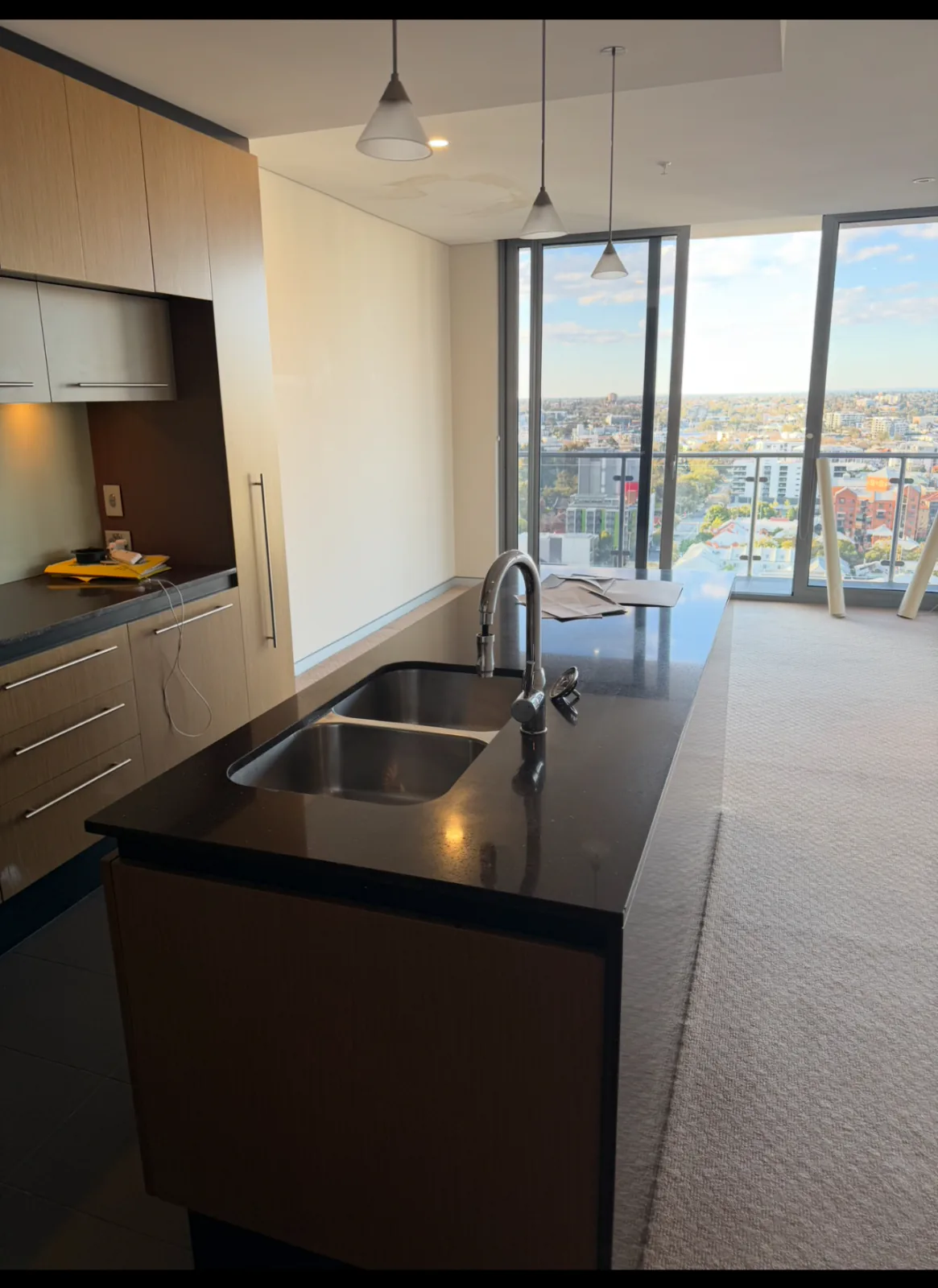 Vacant apartment kitchen with a dark stone island bench, double sink and floor to ceiling windows over the city after a bond clean in Perth