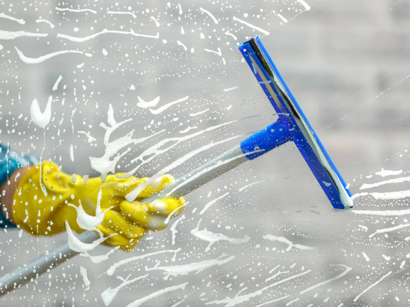 Close up of a gloved hand drawing a squeegee down a soapy window pane
